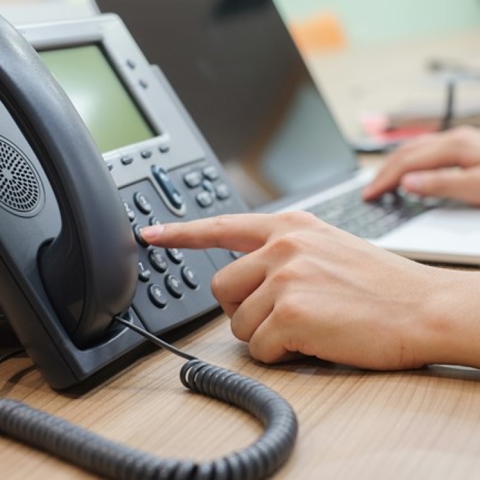A person's hand pressing buttons on an office desk phone
