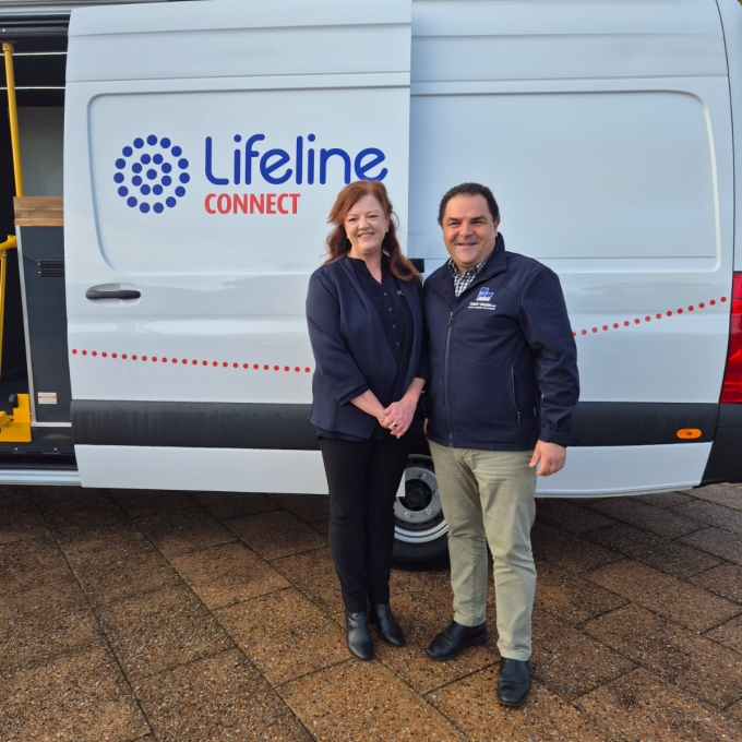 A smiling woman with auburn hair and a man in a navy jacket stand in front of a white Lifeline Connect van with its sliding door open.