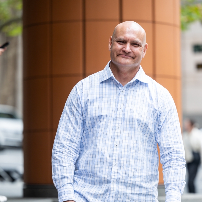Andrew Bacon, in business casual attire, standing on the steps of an office building in Sydney CBD